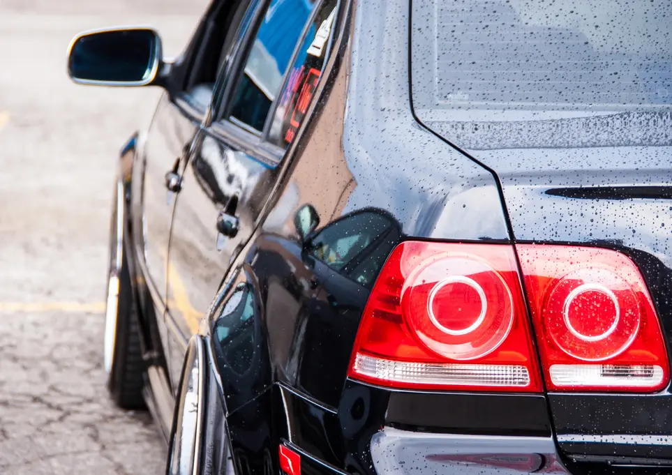 Black car with wet rear, prominent red tail lights, and lowered stance.