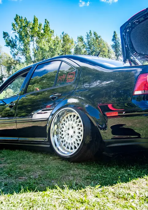 Black lowered sedan with custom wheels and open trunk on grass.