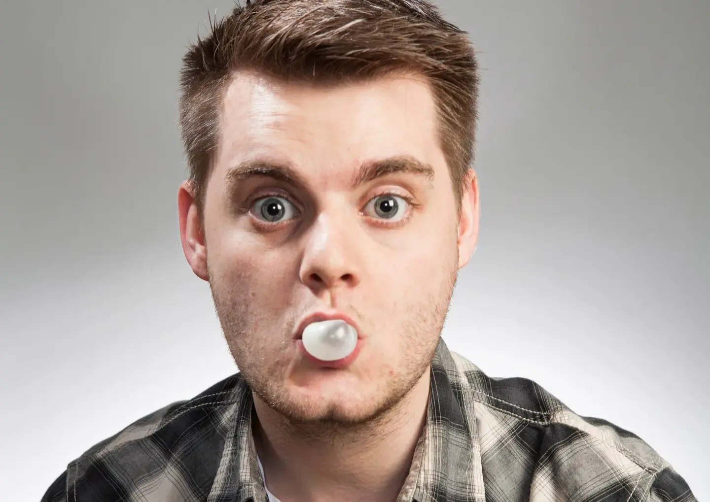 Traditional Portraits by Blake Ferguson Photography depicts a head and shoulders Image of a Male Model wearing plaid and blowing a bubble with gum captured in the Studio.