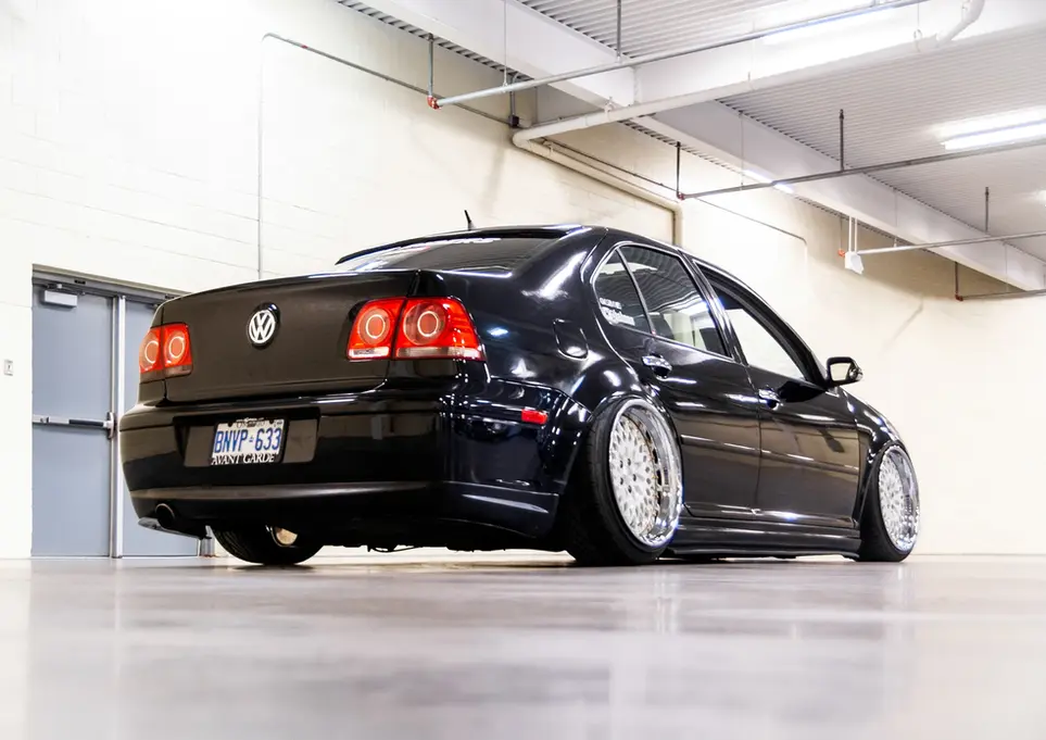 Black Volkswagen Jetta parked in an indoor hall, with chrome wheels.