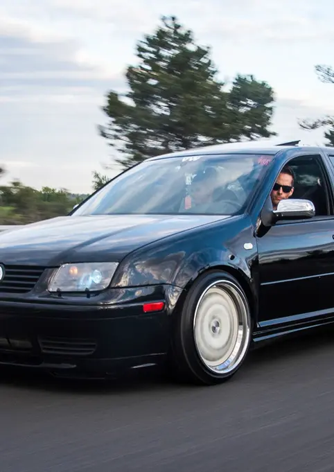 Black Volkswagen Jetta sedan, lowered with aftermarket wheels, on road.