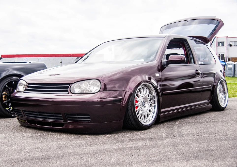Dark purple Volkswagen Golf low-rider, open trunk, custom chrome wheels.