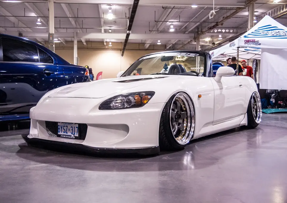 White lowered Honda S2000 convertible at an indoor car show.