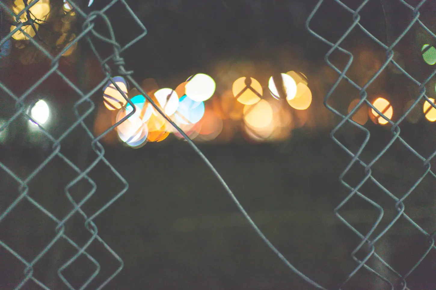 Night & Cityscape Fine-Art Photography by Blake Ferguson depicts bokeh of light shining through a hole in the fence of Downtown London, Ontario, Canada.