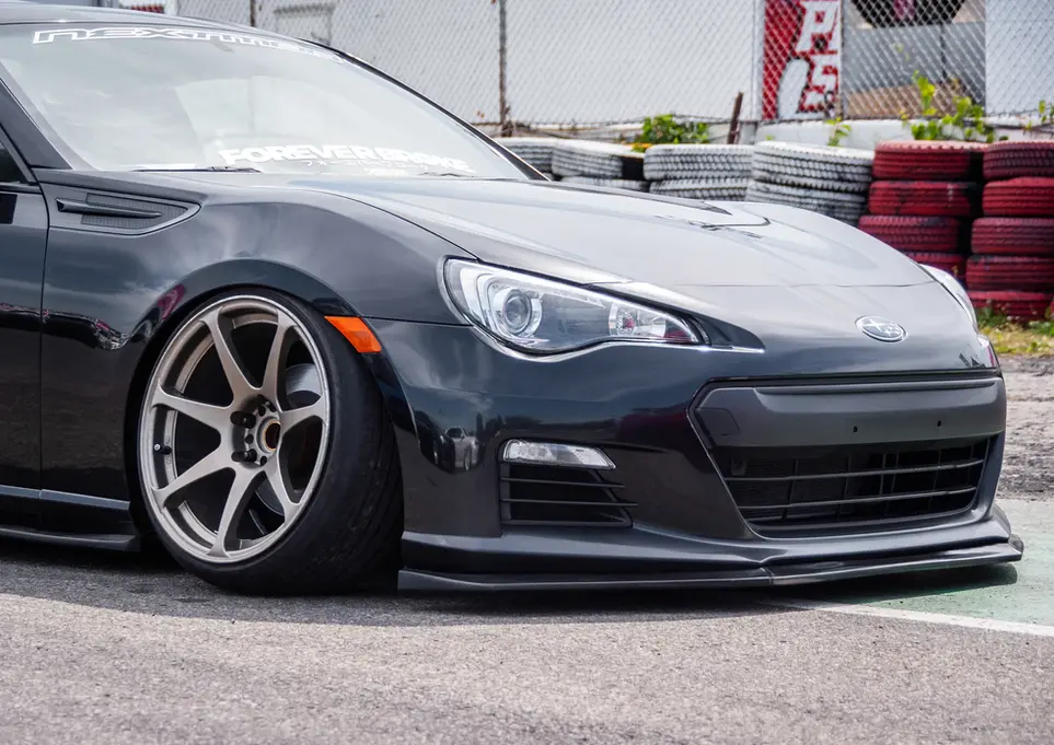 Dark gray lowered sports car parked on a track, tires behind.