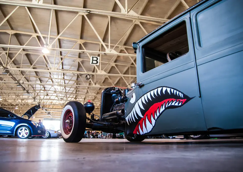 Custom gray rat rod truck with shark mouth art inside hangar.