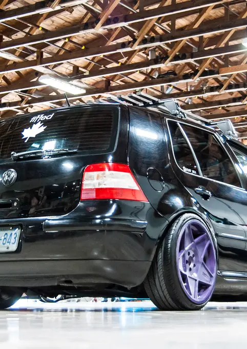 Slammed black Volkswagen Golf Mk4 with custom purple wheels at show.