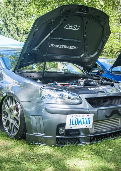 Modified dark gray Volkswagen car, ILOVWUB plate, hood open at car show.