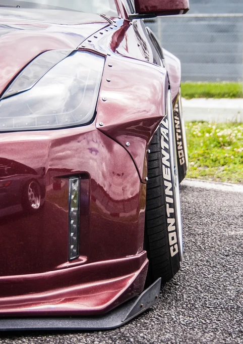Customized red car with widebody fender, 'CONTINENTAL' tire on racetrack.