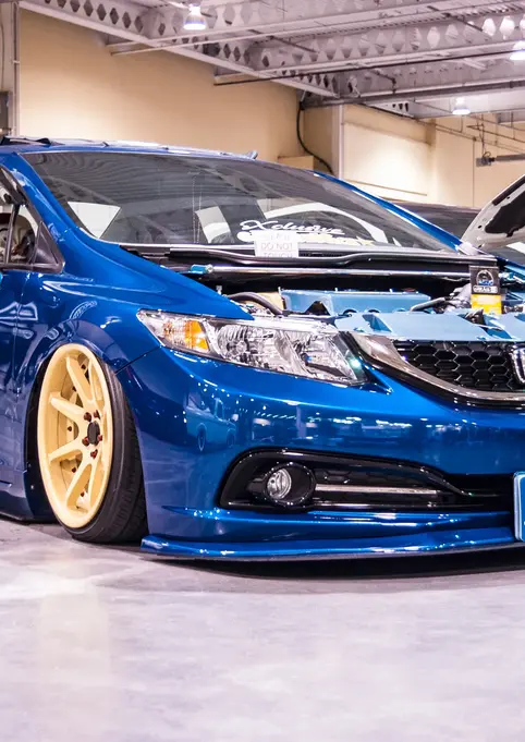 Lowered blue Honda Civic, "JCLUSIVE" plate, gold wheels, open hood.