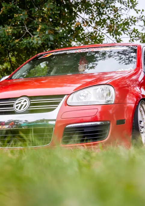 Red Volkswagen vehicle parked in grassy field with chrome details.