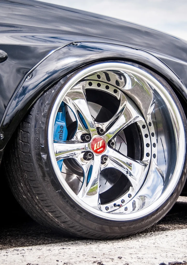 Lowered black car, chrome wheel, blue caliper, "TOITURE LOCATION" sign.