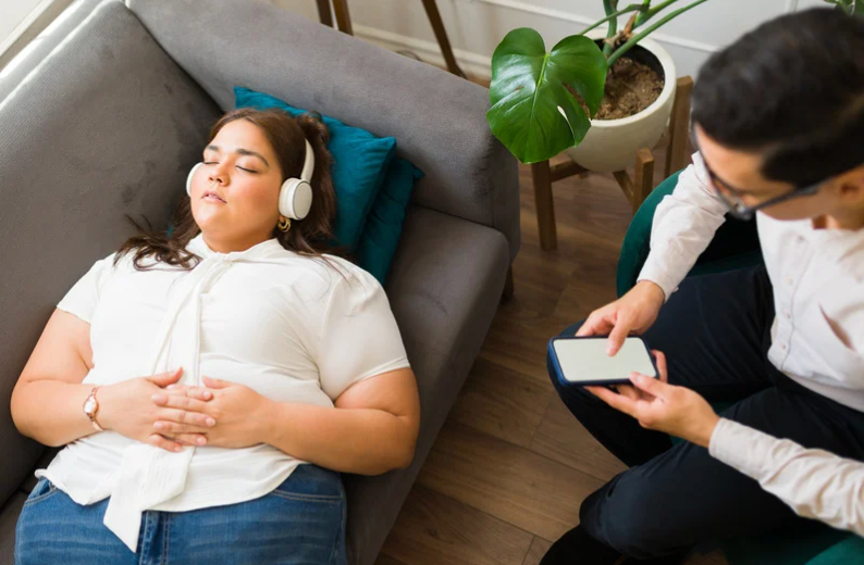 A person with headphones lying on a couch while someone else leads them through a guided meditation