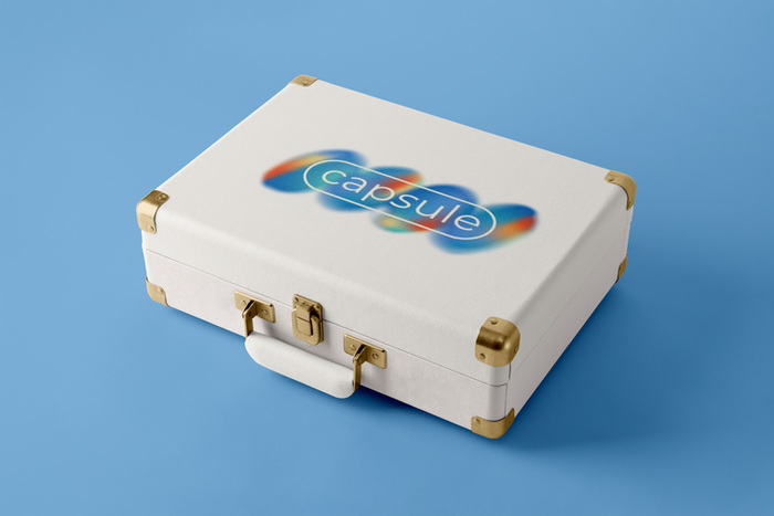 White Capsule premium suitcase with rounded edges, gold hardware, and Capsule gradient logo displayed on a blue background.