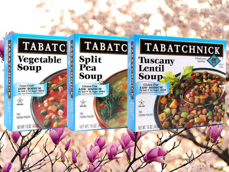 Three low sodium frozen soups on a background of trees with purple flowers in bloom