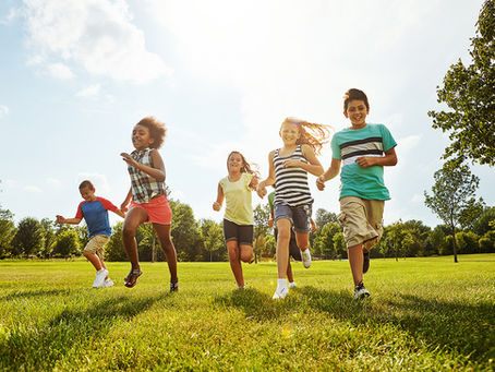six young people smiling while running through a park, dressed in shorts on a sunny day