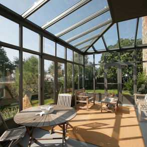 Sunlit sunroom patio with floor-to-ceiling glass walls and outdoor furniture in a bright, open space