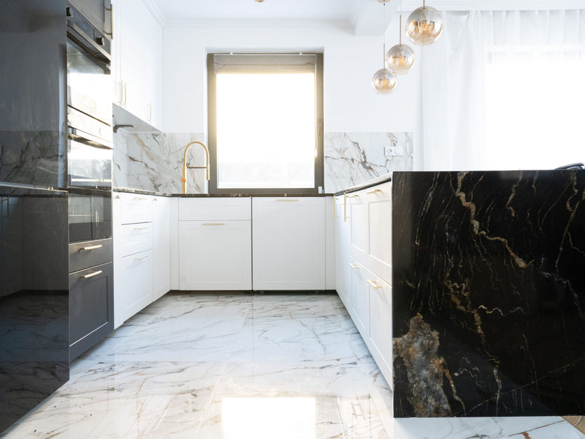 Luxury kitchen by Marble World Africa featuring polished white marble tiles with grey veining, a bold black marble island, and gold accents for a timeless, high-end finish.