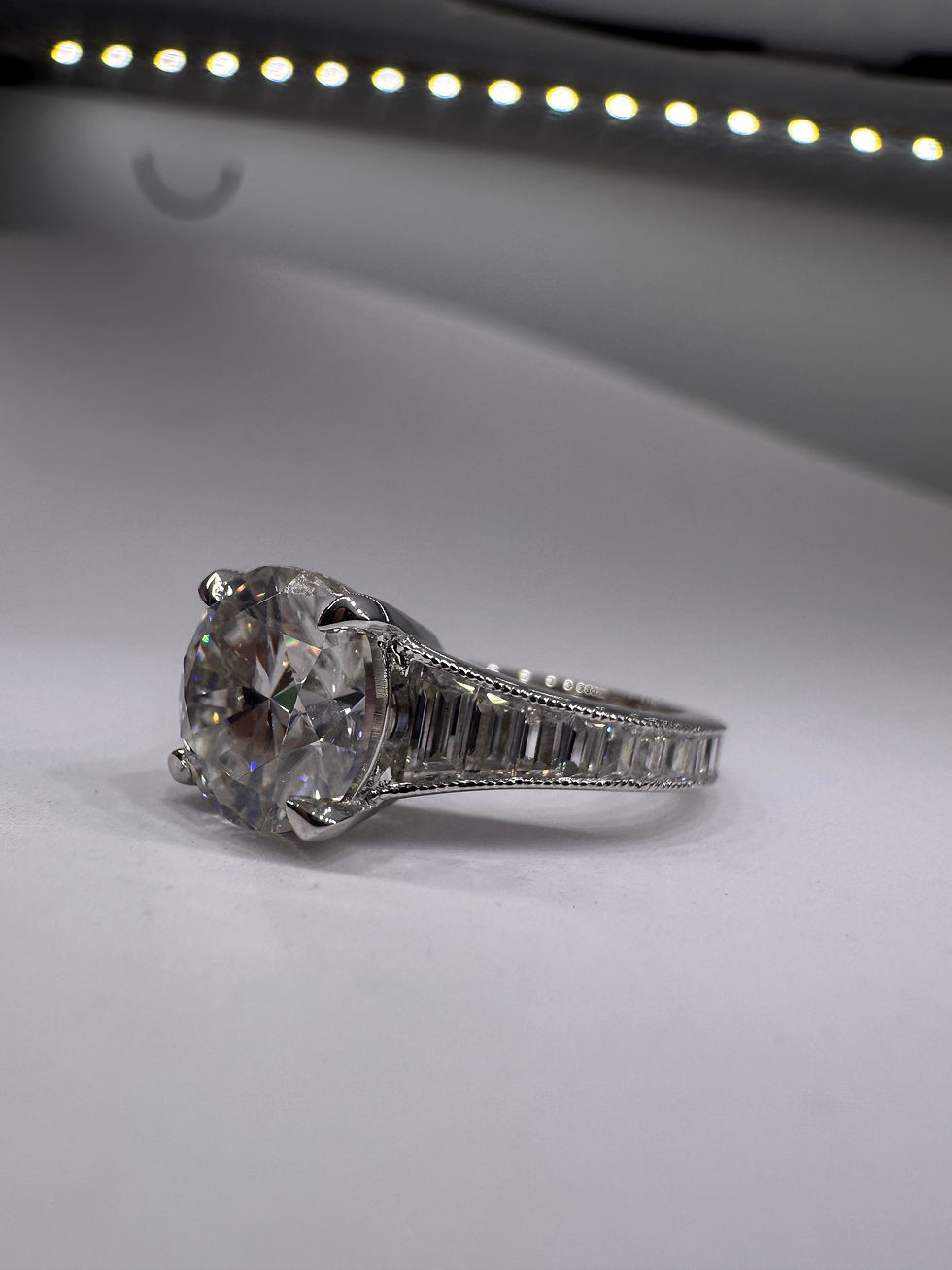 Thumbnail: 3 carat round moissanite with graduated trapezoids on a milgrain band 