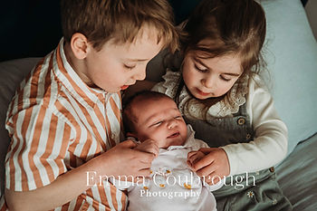 Siblings holding newborn baby on bed