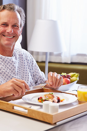 Male Patient In Hospital Bed Eating Meal From Tray.jpg