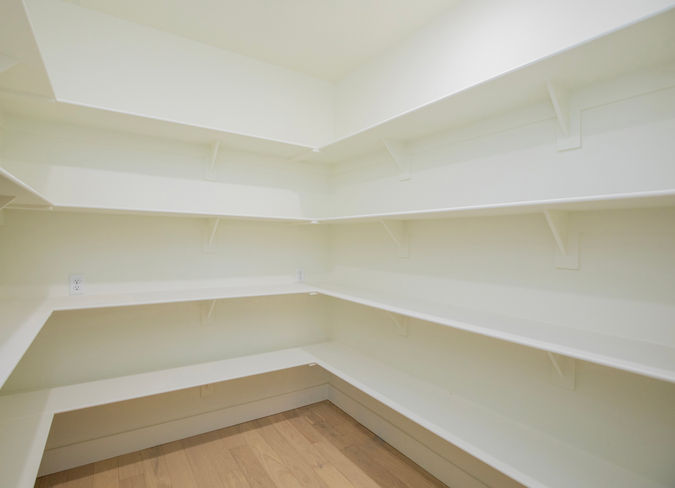 Storage room with honey-toned wood flooring and ample white built-in shelving.