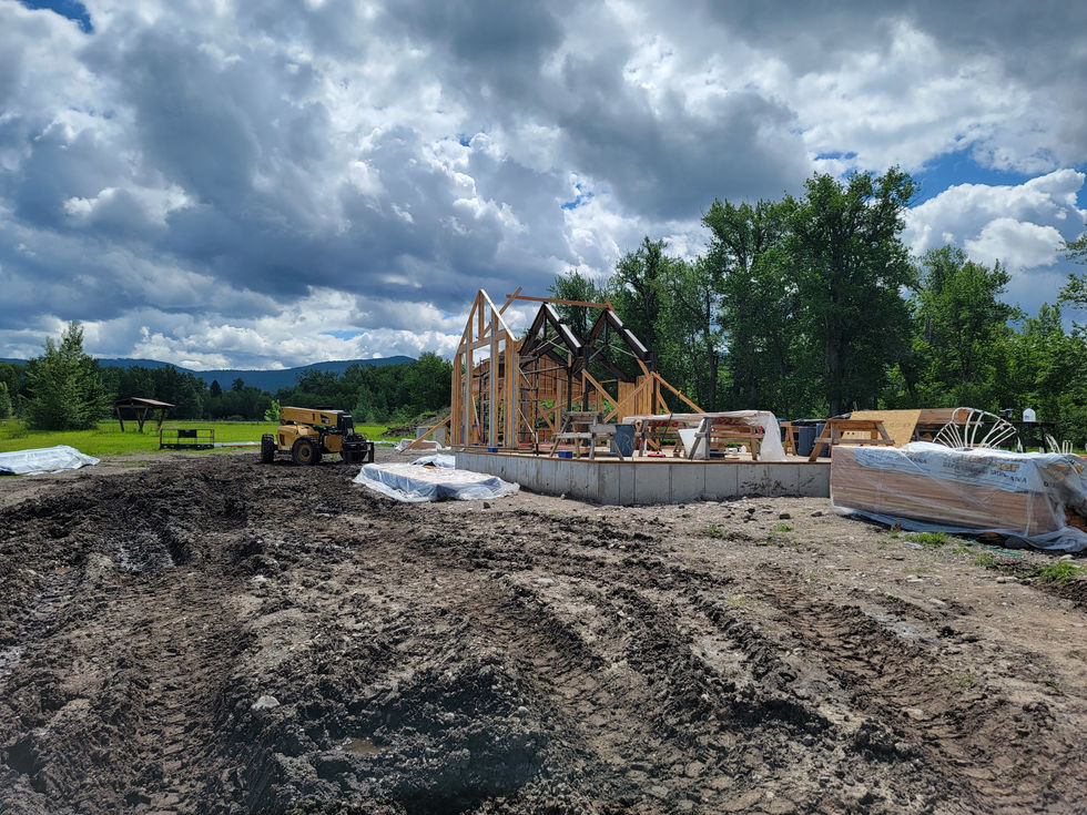 Timber frame shell standing on a new foundation with freshly graded ground and mountains behind in Bozeman