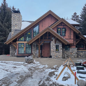 A large house with river rock on the chimney and entry, windows installed and snow across the yard in Cameron, Montana