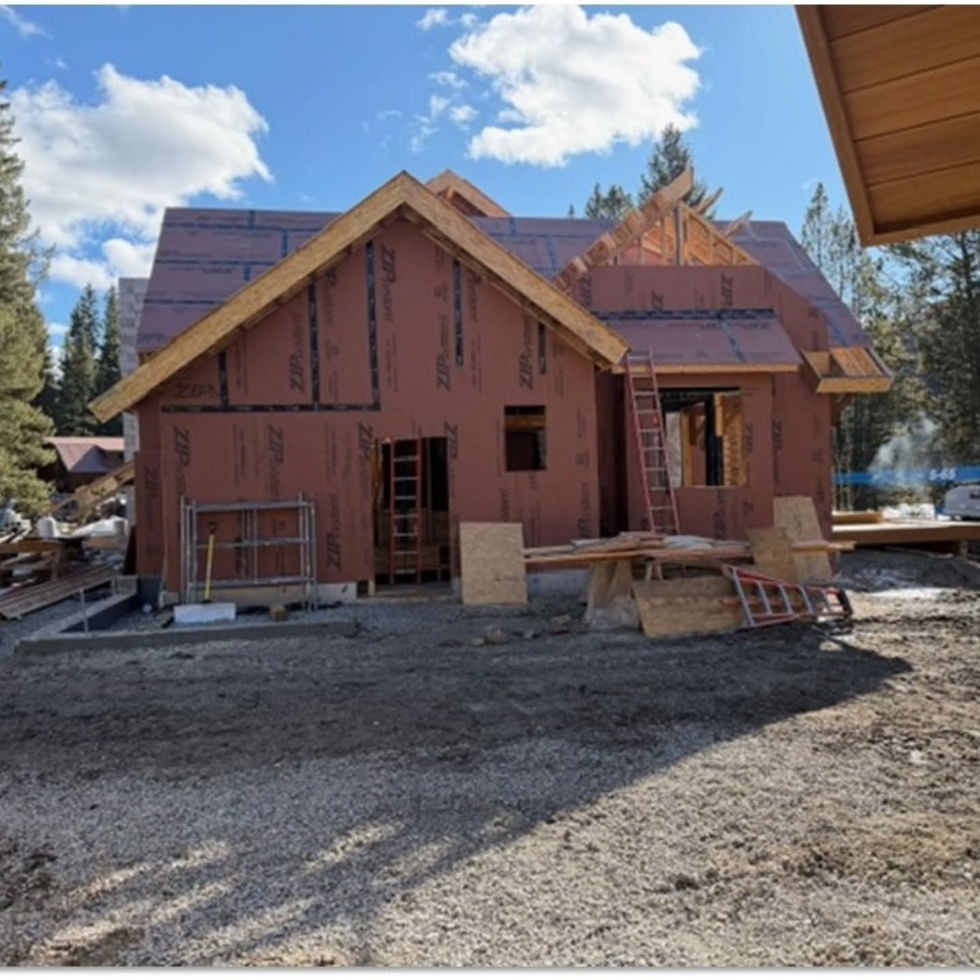 A smaller sheathed building with a steep gable, leaning ladders and a lumber bench on a gravel yard in Cameron, MT
