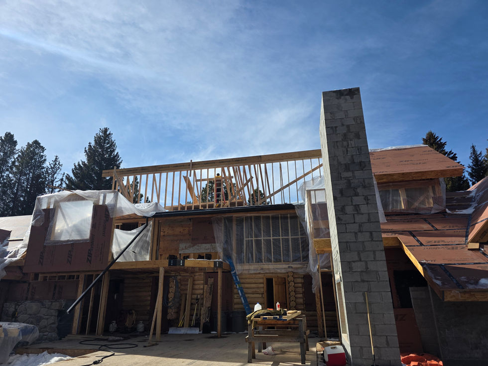 Rafters being set along a ridge above wrapped dormers and a tall block chimney in Ennis, Montana