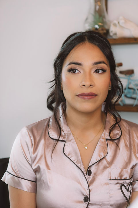 Soft glam makeup on a bridesmaid, featuring radiant skin, warm neutral eyeshadow, defined lashes, and a nude glossy lip, photographed indoors during wedding prep.