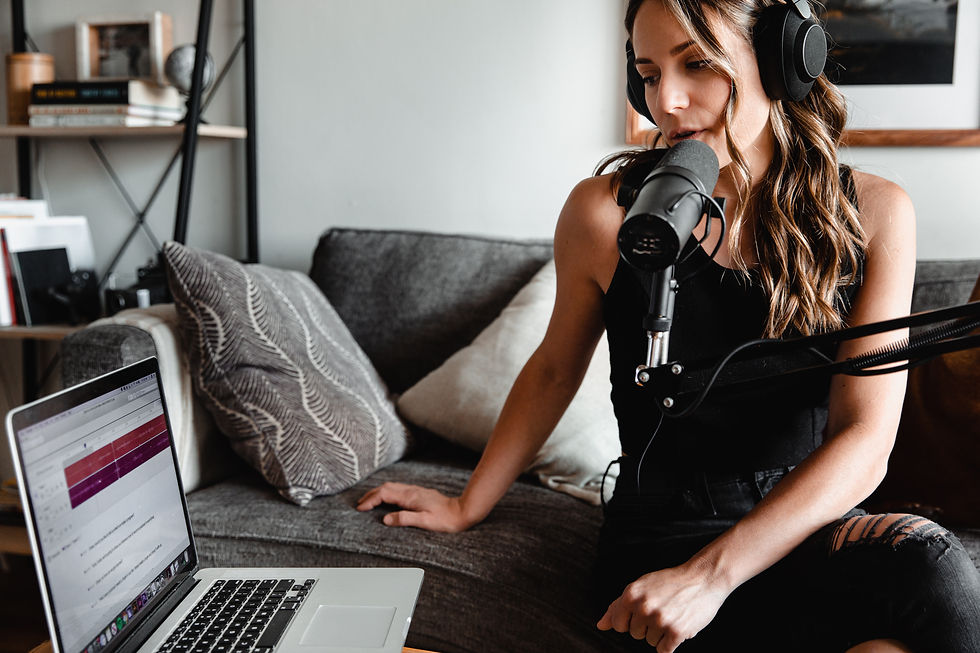 Woman with headphones records a podcast on a sofa with a mic and laptop after taking the "How to launch a podcast with a feeling, a phone & a few dollars" course.