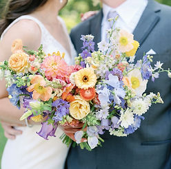 A bride and groom stand together holding a bridal bouquet full of local orange and purple blooms.