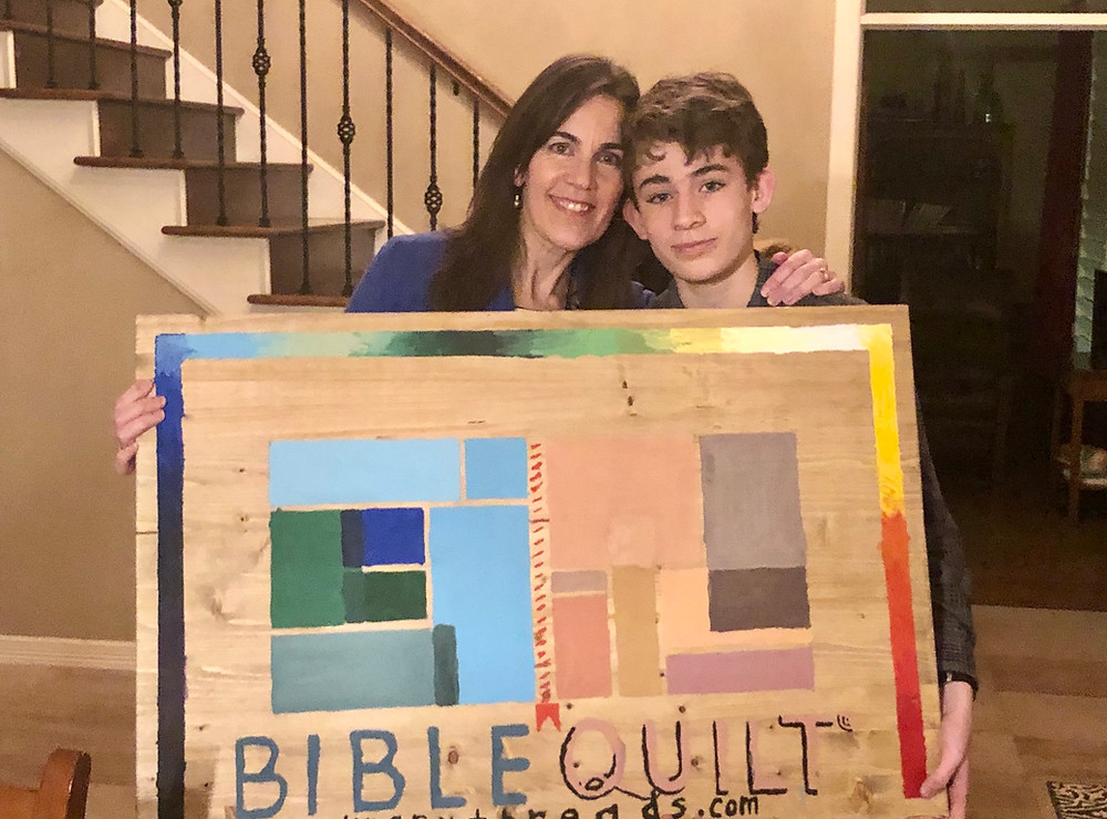 Di & son with painted Bible Quilt Journal logo sign