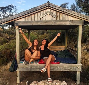 Two women joyfully pose in a wooden shelter