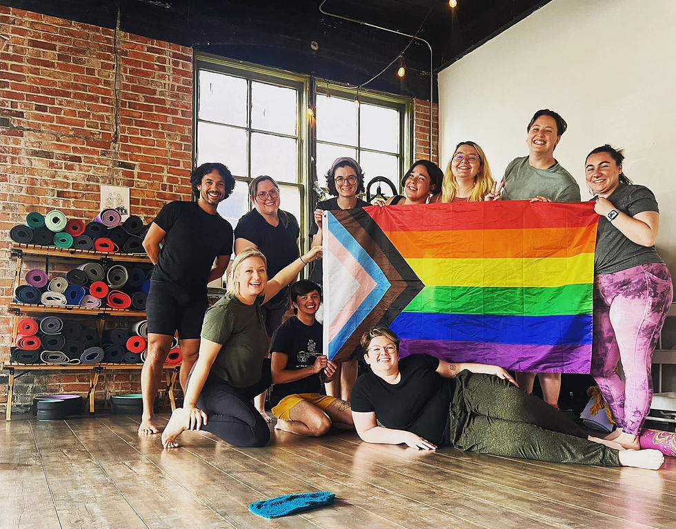 9 adult queer students happily holding up a pride flag after class in the kby studio