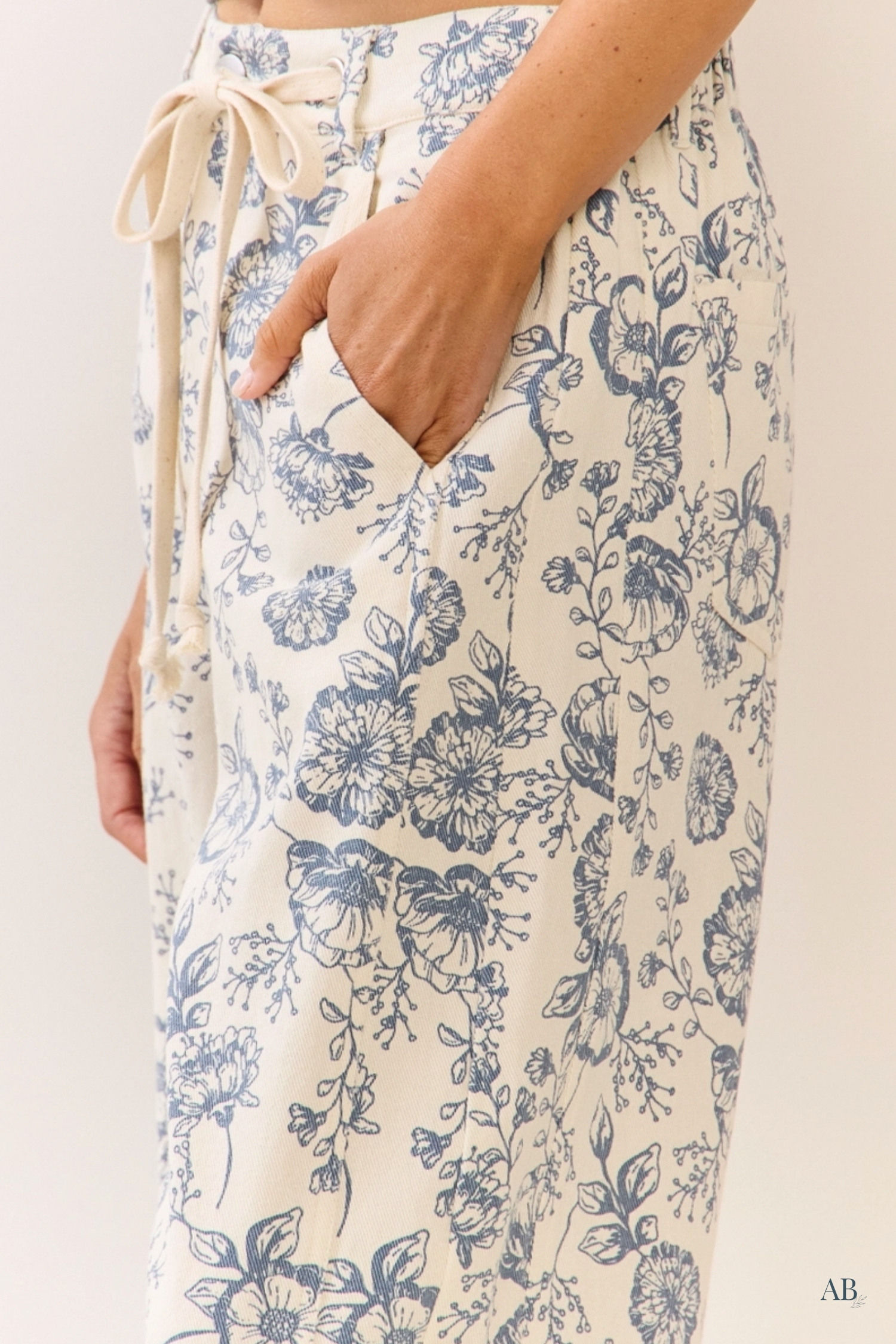 Close up of functional side pocket on cream cotton blend pants showcasing a detailed vintage blue floral pattern.