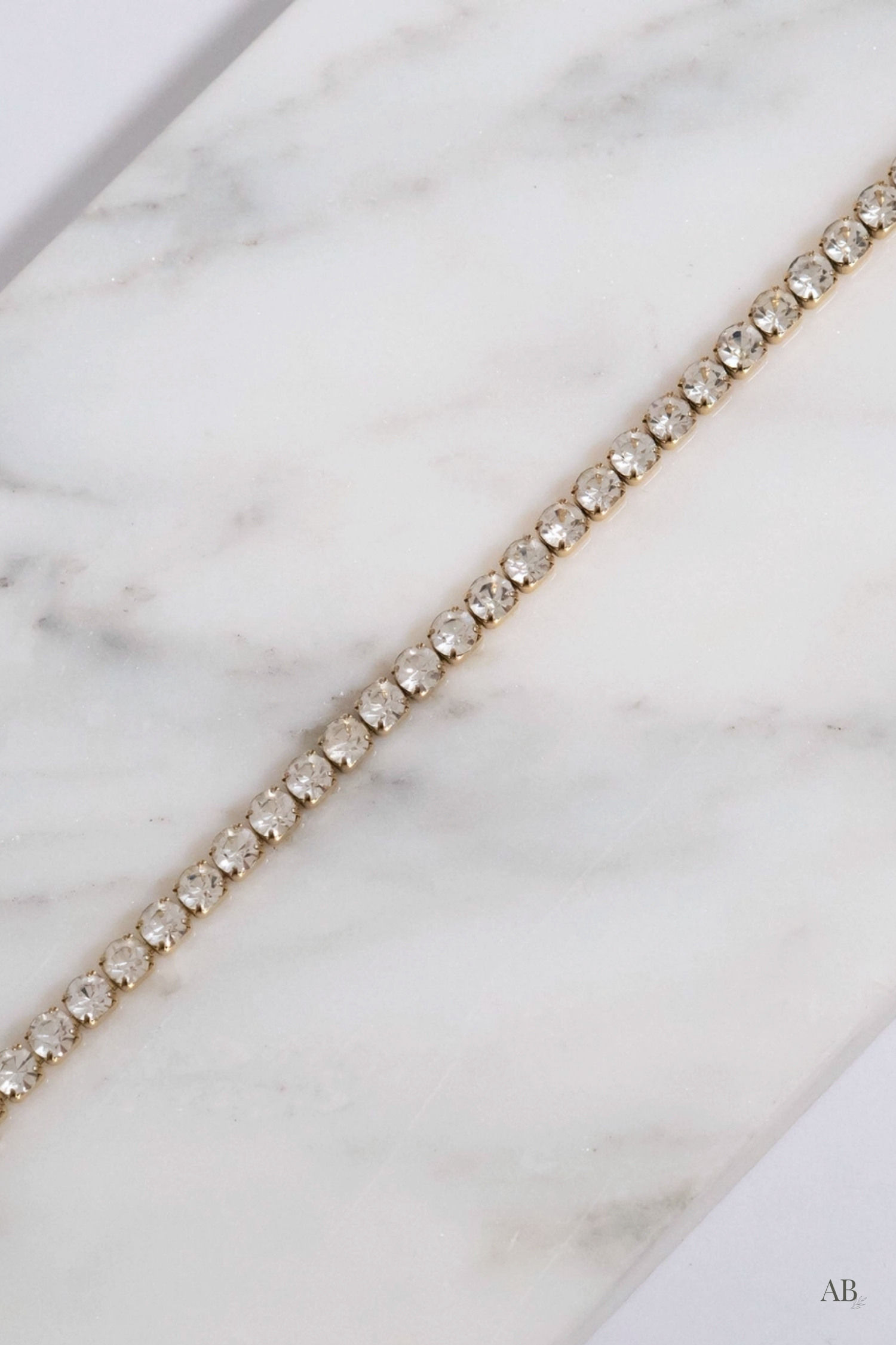 Macro detail view of a hypoallergenic 18k gold coated stainless steel tennis bracelet resting on white marble.