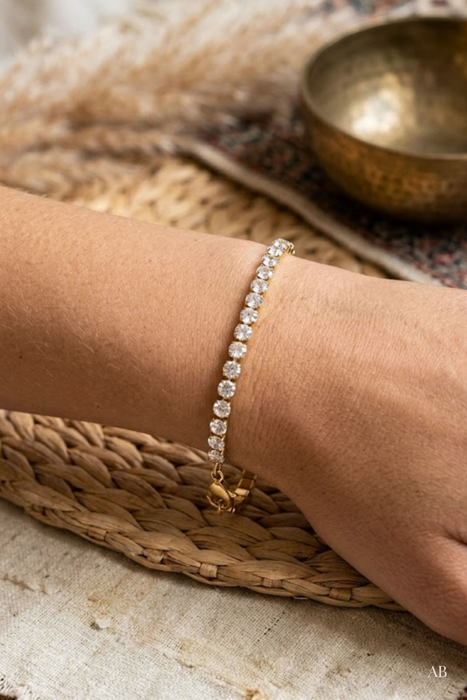 Close-up of a model wearing a tarnish-free gold tennis bracelet with 3mm cubic zirconia stones on a woven mat.
