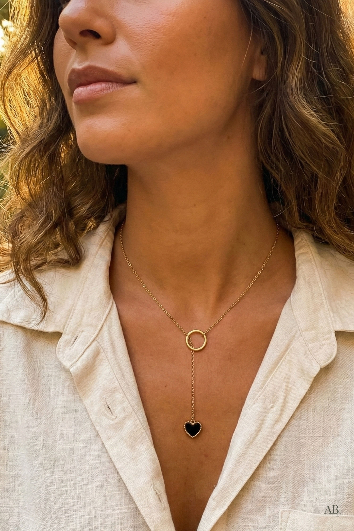 Close-up of a model wearing a gold lariat necklace with a black heart pendant and a linen button-down shirt.