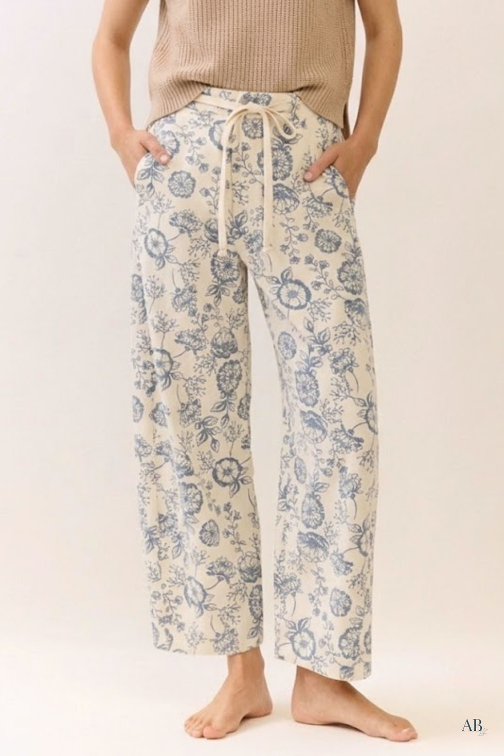 Model wearing cream straight leg cropped pants with blue floral print, side pockets, and cream drawstring waist.