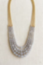 Gold-tone multi-chain lavender necklace with layered strands of faceted beads, statement jewelry on neutral fabric.