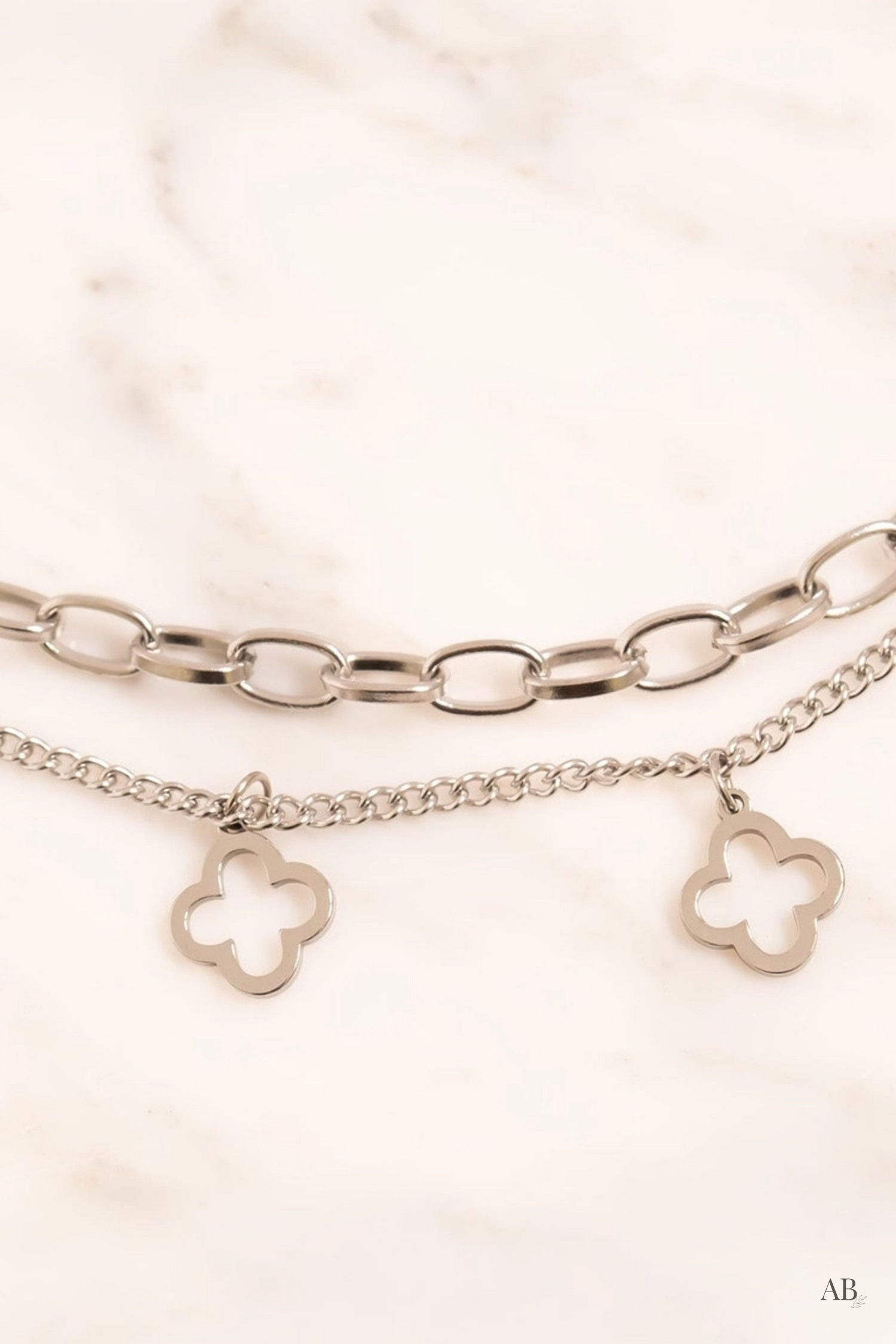 Close-up of a tarnish-free silver layering charm bracelet with clover silhouettes.