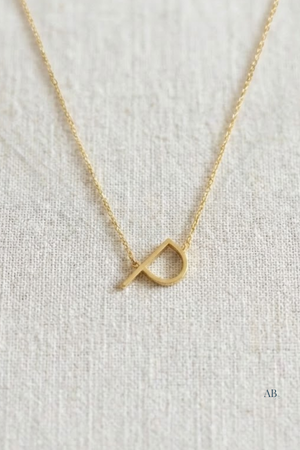 Gold vermeil sideways initial necklace letter P on neutral fabric background, modern personalized jewelry detail.