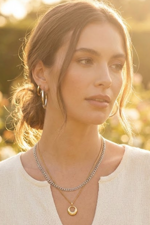 Woman wearing mixed-metal layered necklaces and hoop earrings in soft golden sunlight, showcasing simple, high-quality everyday jewelry.