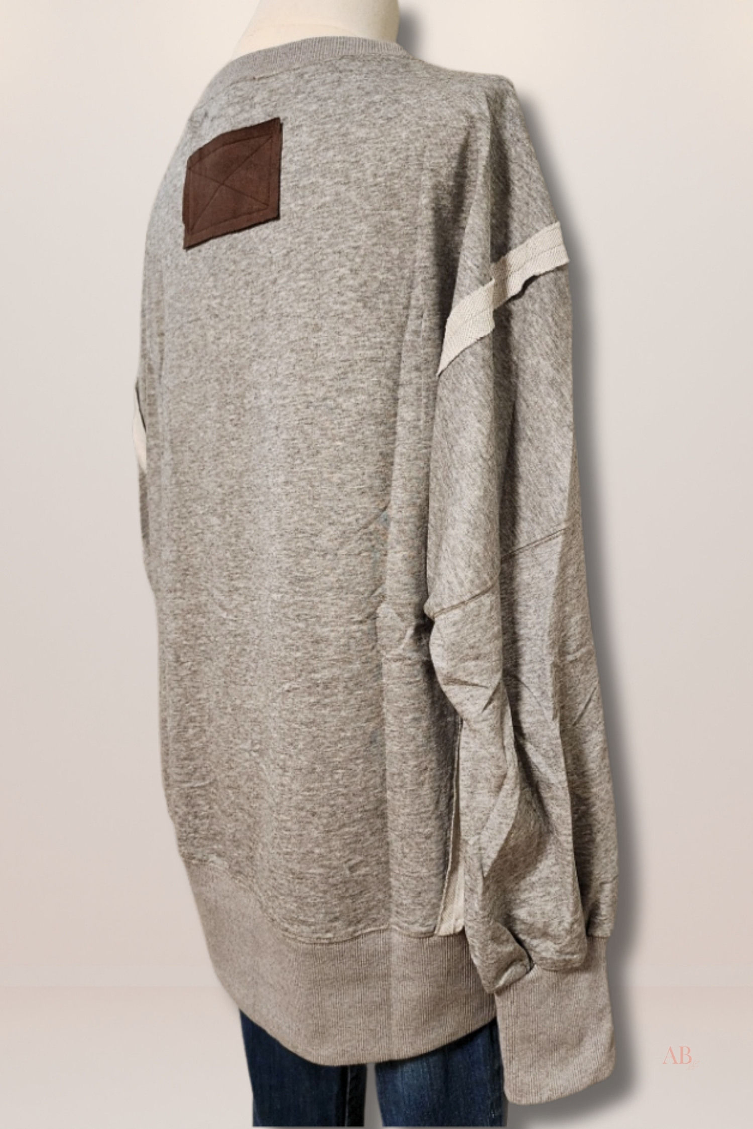 Rear view of an oversized grey sweatshirt highlighting a small brown faux-suede accent patch stitched below the back collar.