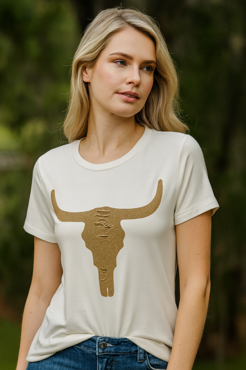 White t-shirt with gold longhorn skull graphic, modeled outdoors against greenery.