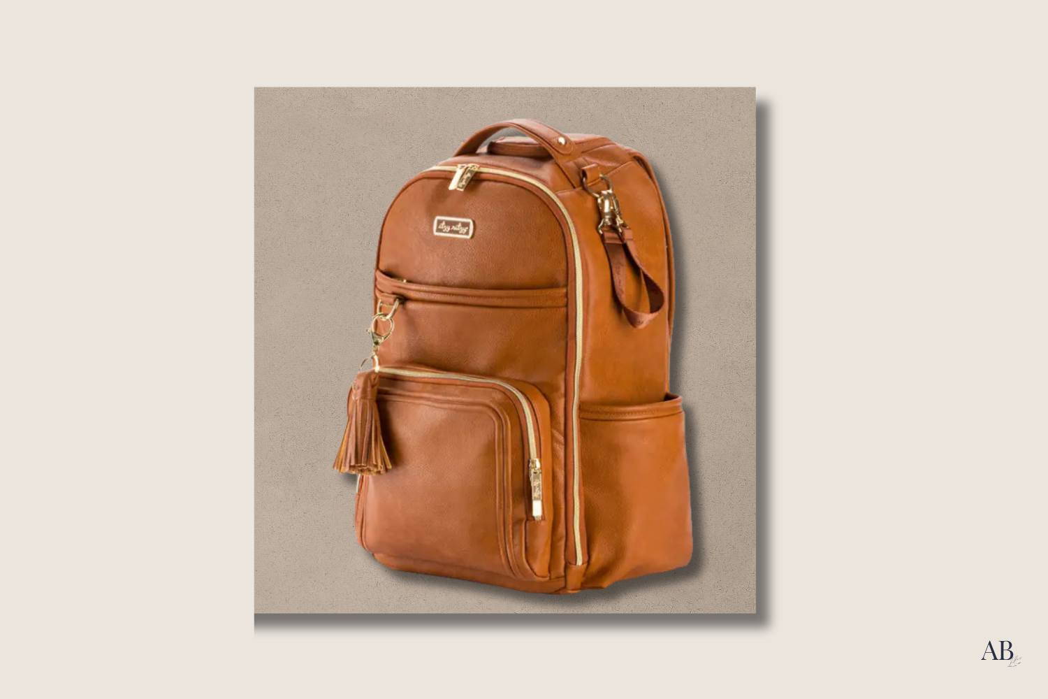 Angled front view of Itzy Ritzy Cognac Boss Plus Backpack showing tassel and front compartments