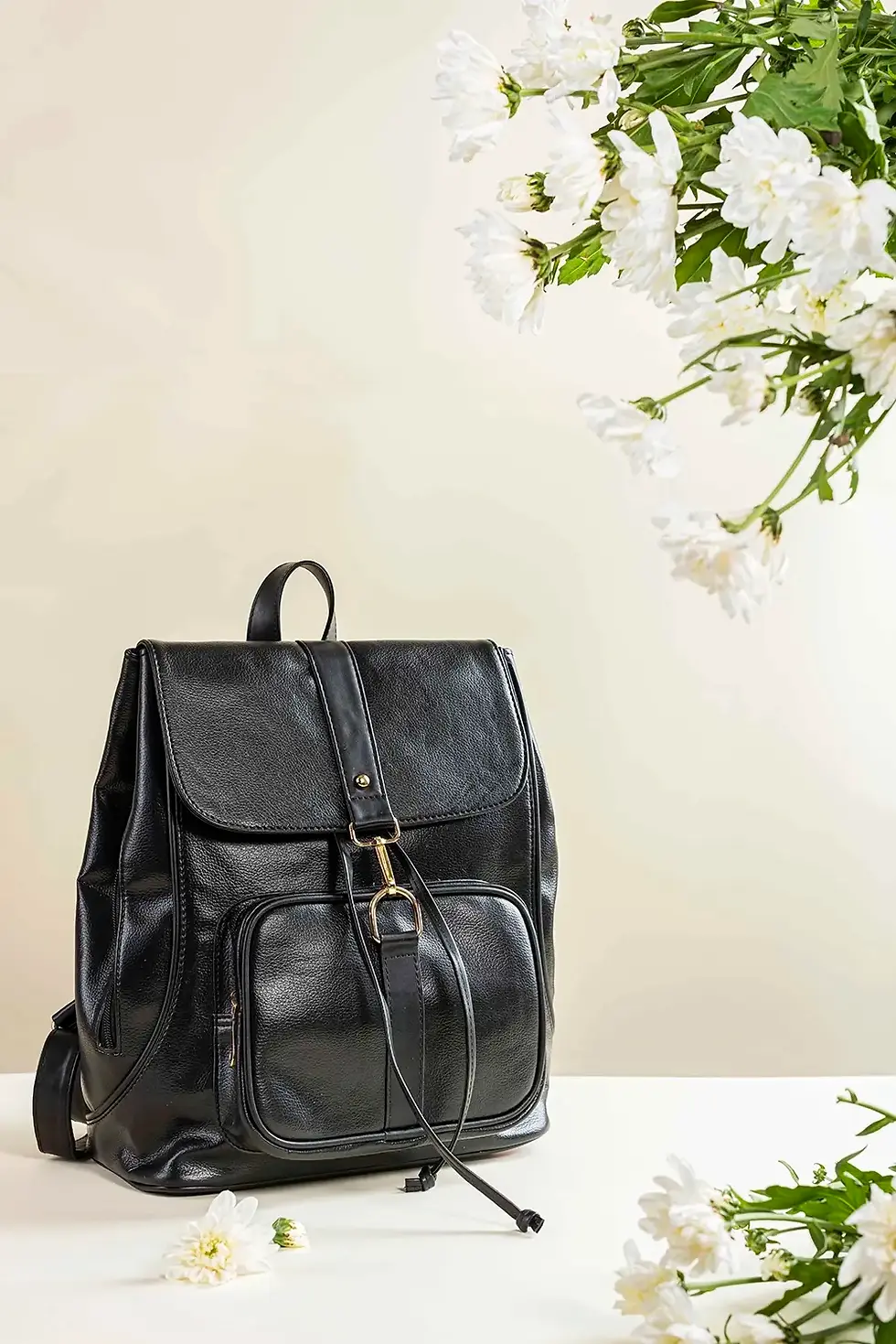 black leather bag with a structured silhoutte. minimal studio setup with soft lighting and white floral accent.