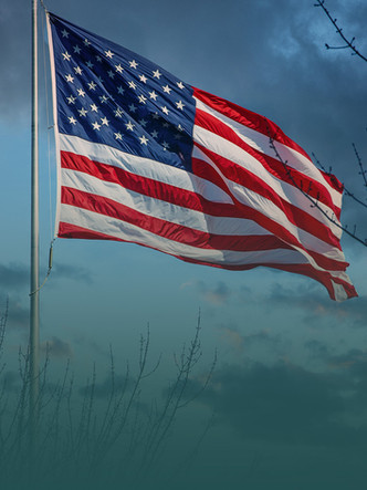 American flag flying on a flagpole against a dark, cloudy sky.